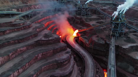 aerial view of a large industrial open-pit mining operation with smoke and molten material