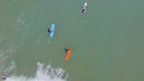 Birdseye-view-of-longboard-surfers-duck-dive-or-turtle-below-crashing-wave