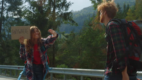 emotional hitchhikers waving hands on mountain road. couple hold placard sign.