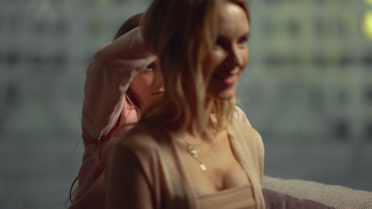 소파에서 엄마의 머리카락을 하고 있는 소녀. 엄마와 딸이 실내 소파에 앉아 있다.