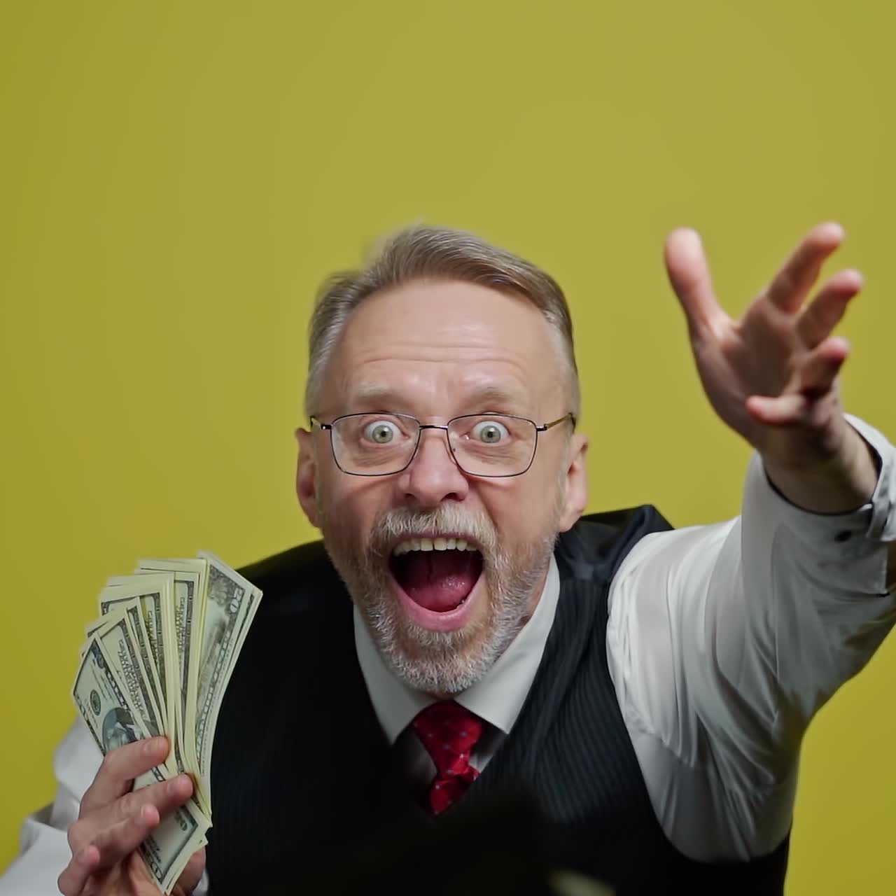 Happy elderly man throwing money. Mature man in glasses with grey hair holding dollar banknotes and throws into the air indoors. Slow motion.