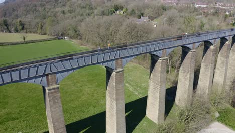 people walk across the beautiful narrow boat canal route called the pontcysyllte aqueduct famously designed by thomas telford, located in the beautiful welsh countryside, a huge bridge viaduct