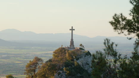 Ein-Hügel-Am-Santuari-De-San-Salvador-Auf-Mallorca,-Spanien,-Gekrönt-Von-Einem-Kreuz,-Mit-Einer-Bergkette,-Die-Am-Späten-Nachmittag-Eine-Majestätische-Kulisse-Bildet