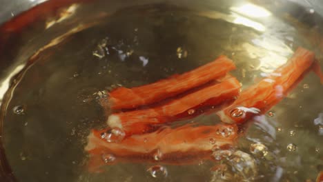 close up of surimi sticks dropped into the boiling soup pot. sukiyaki or shabu