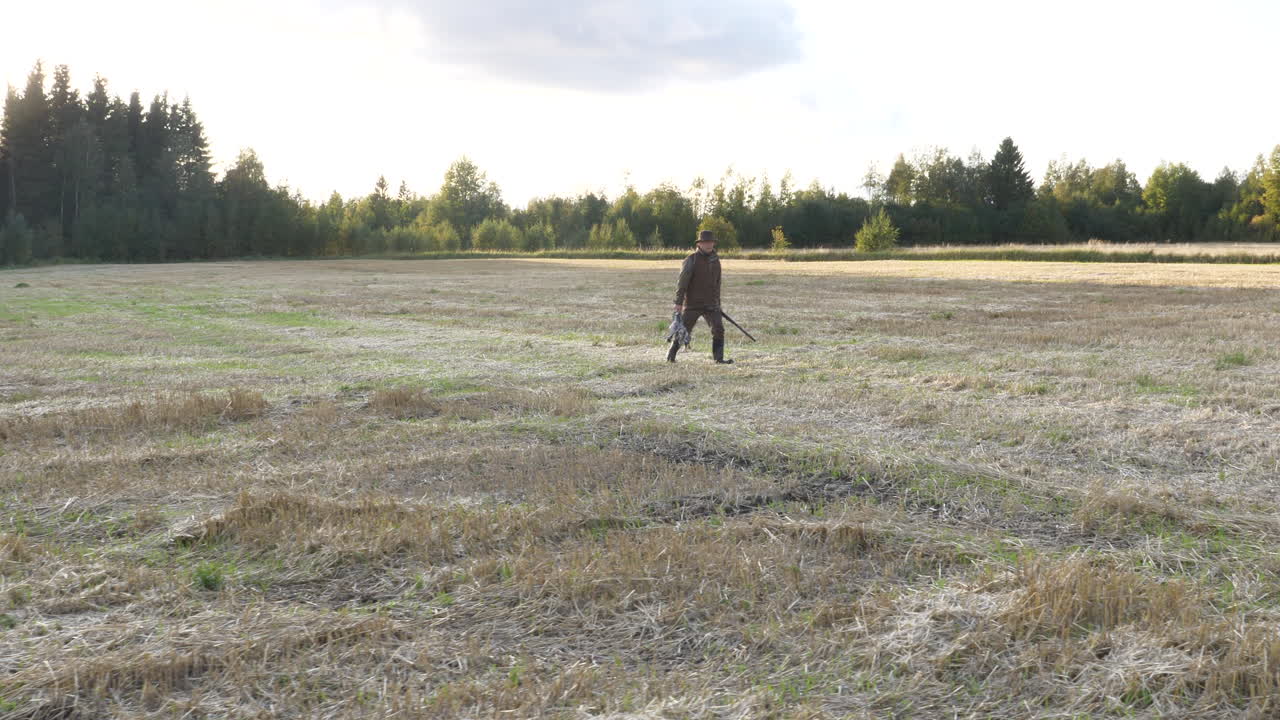 cazador caminando en el campo llevando pájaros y rifle en sus manos, una recompensa de cazadores después de un largo día en el bosque