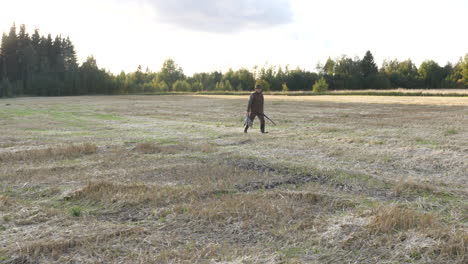 Hunter-walking-on-field-carrying-birds-and-rifle-in-his-hands,-a-hunters-reward-after-a-long-day-in-the-forest