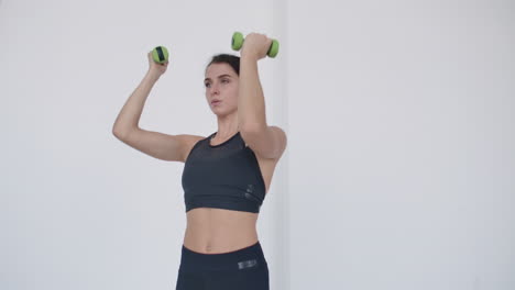 basic exercise for the deltoid muscle: a young caucasian woman lifts dumbbells for arm and shoulder exercises. lift dumbbells over your head