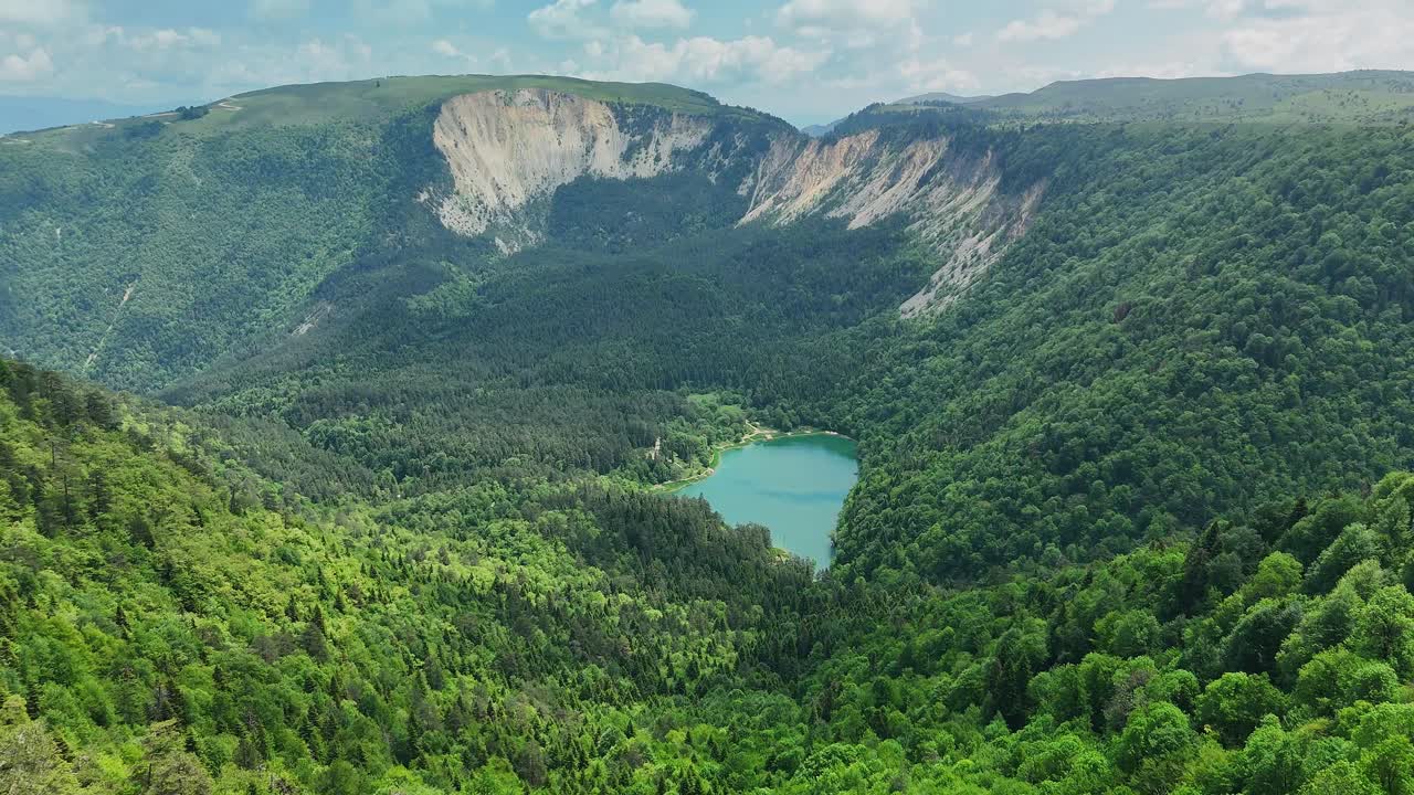 Paesaggio montano sereno con una lussureggiante foresta verde e un lago blu sottostante.