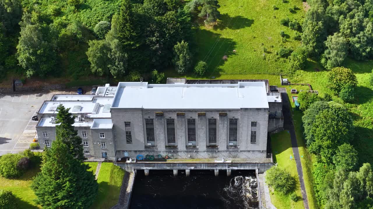Drone footage reveals hydroelectric power station surrounded by lush greenery, bright daylight, minimal camera movement
