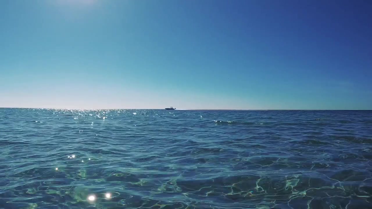 Close up drone view of open sea at eye line with boat moving across the horizon, then panning to the left to the shoreline.