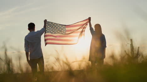 man and woman raising the us flag over a field of wheat at sunset