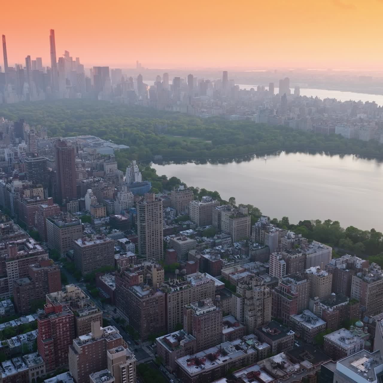 The Pond reflecting skies in the Central Park, New York. Skyscrapers and other buildings in the thin fog. Pink sky at backdrop