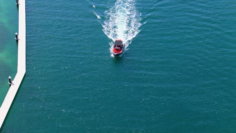 Drone-push-in-tilt-down-as-red-and-black-boat-with-black-tarp-covering-drives-past-pier-in-channel