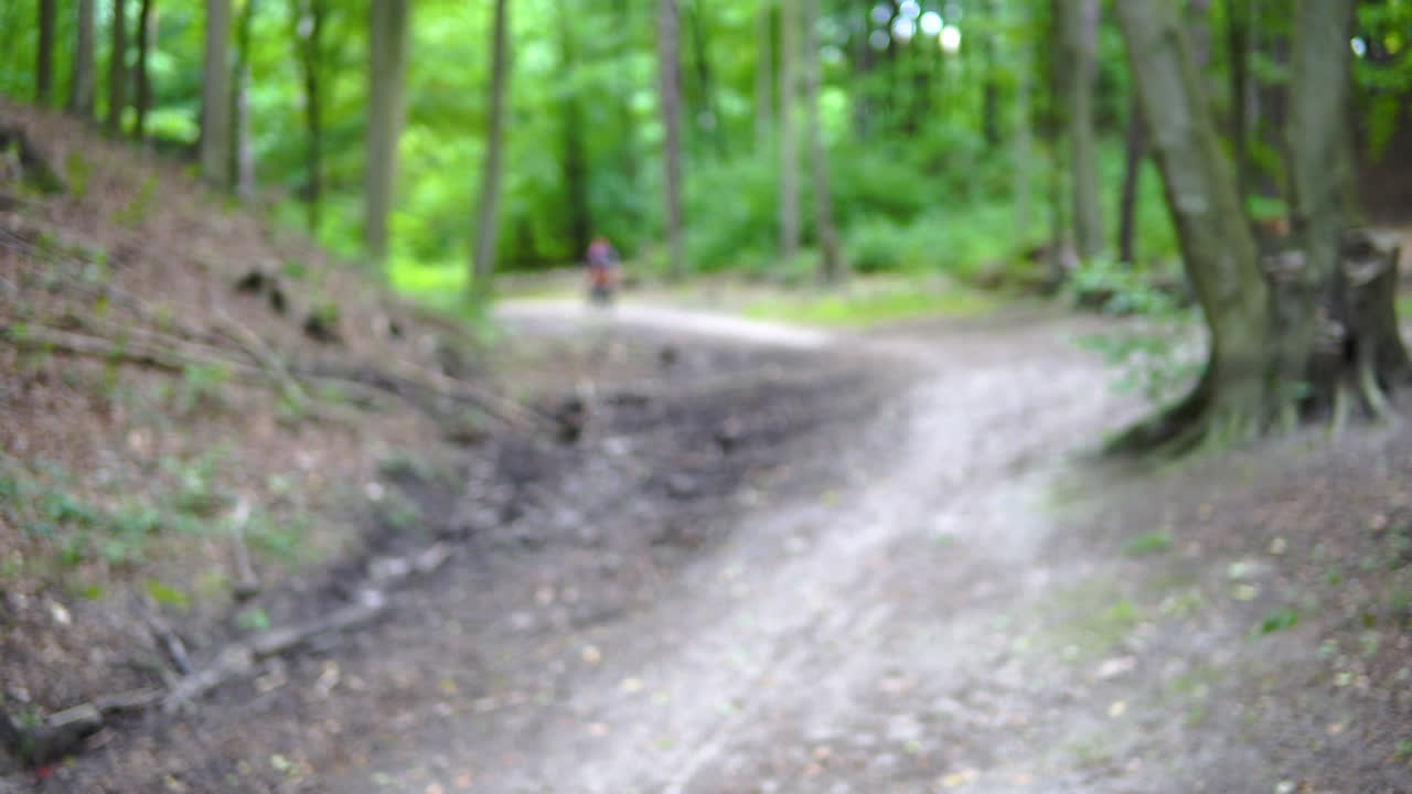 Campo lungo sfocato di un ciclista di mountain bike che pedala su un sentiero nel bosco durante il giorno