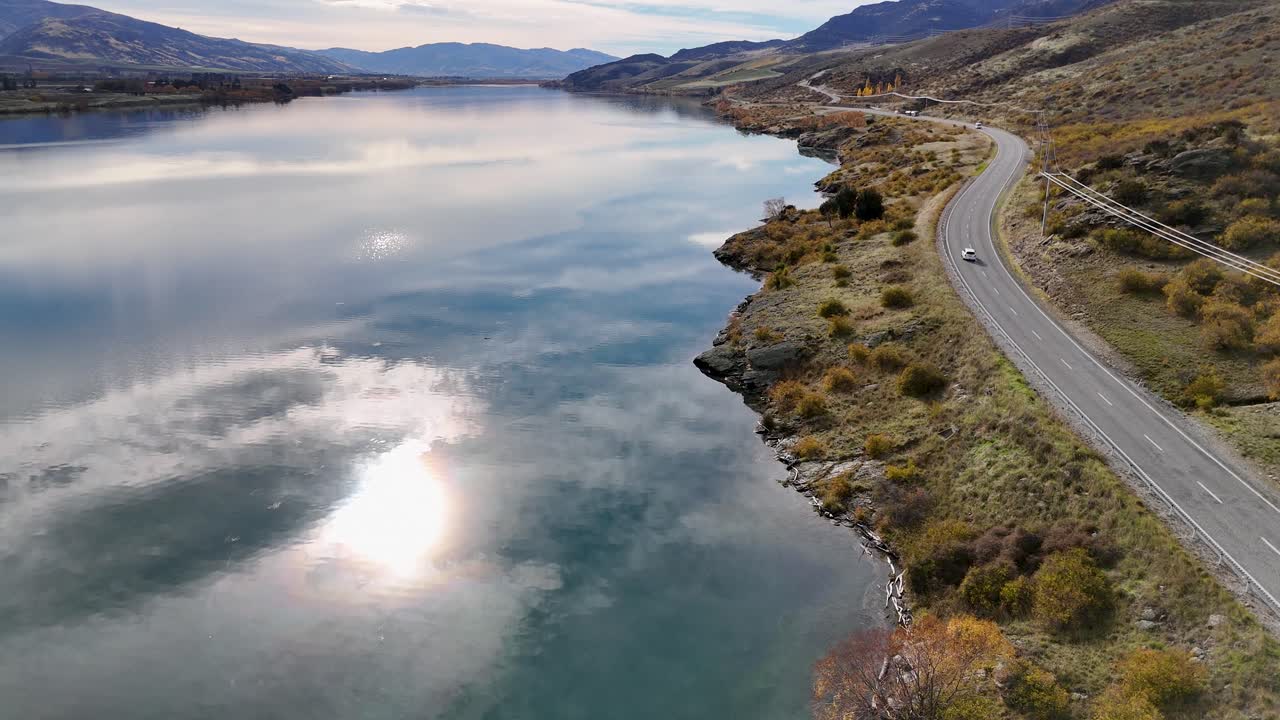 Aerial view of Lake Dunstan with reflective waters and winding road in autumn light, showcasing serene natural beauty