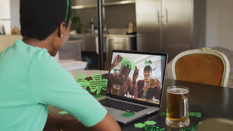 una pareja diversa sonriente con cerveza vistiendo artículos en forma de trébol en una videollamada en una computadora portátil