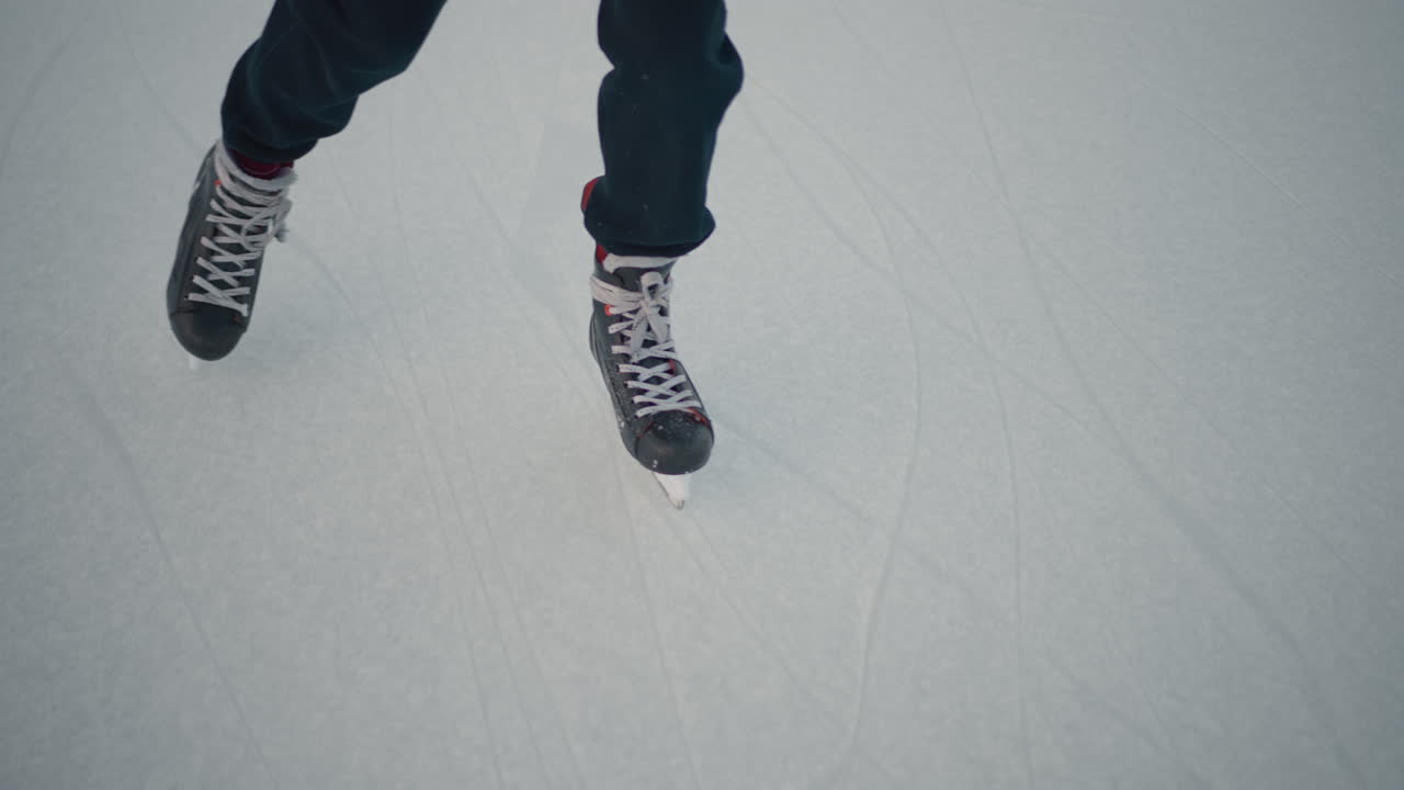 top down view person skating on frozen lake ice surface marked by blade tracks smooth motion capturing skillful glide athletic movement during serene winter day subtle sunlight reflecting on terrain