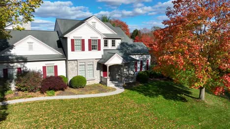 a white house with red shutters and autumn trees