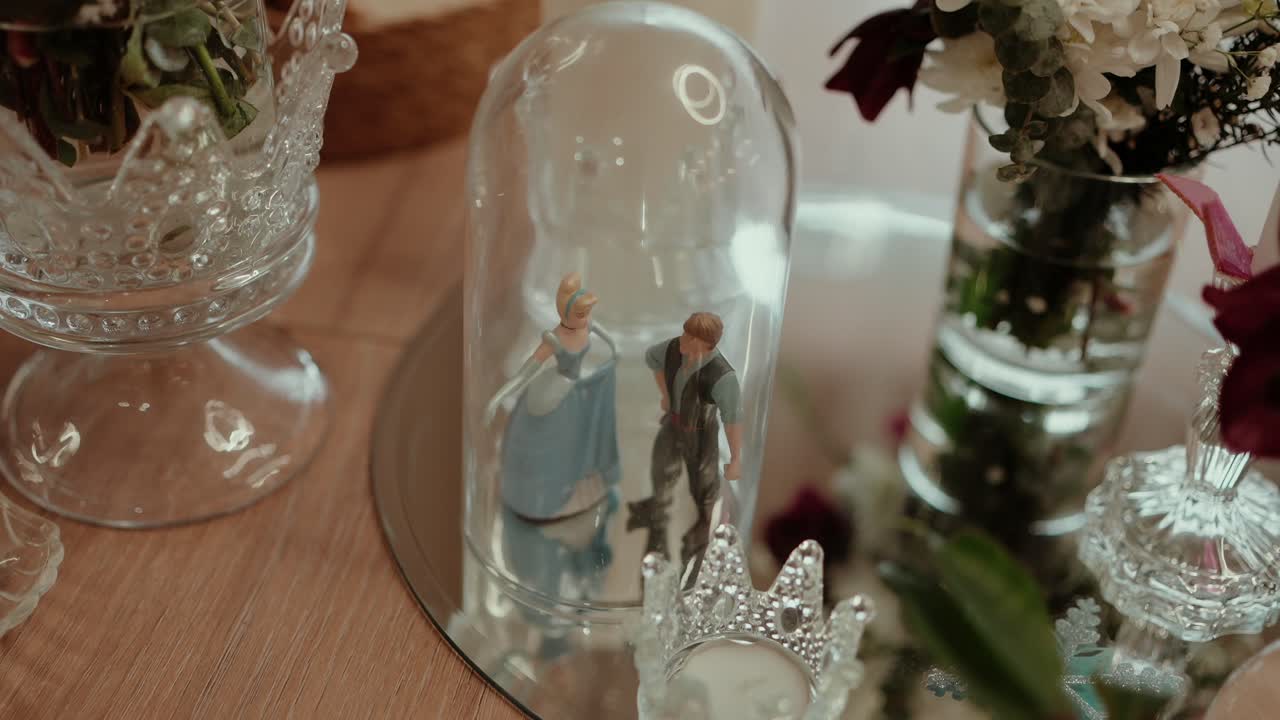 Close view of couple figurines inside glass dome surrounded by flowers decor