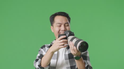 close up of asian photographer looking at the pictures in the camera then screaming goal and dancing to celebrate satisfied with the result while standing on green screen background in the studio