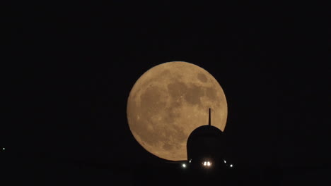 Un-Avión-Pasa-Frente-A-La-Luna-Llena-Al-Acercarse-Para-Aterrizar-En-El-Aeropuerto-Internacional-De-Los-ángeles-En-Cámara-Lenta