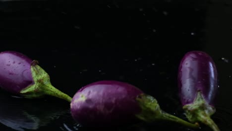 purple eggplants being tossed and tumbling through water on black background