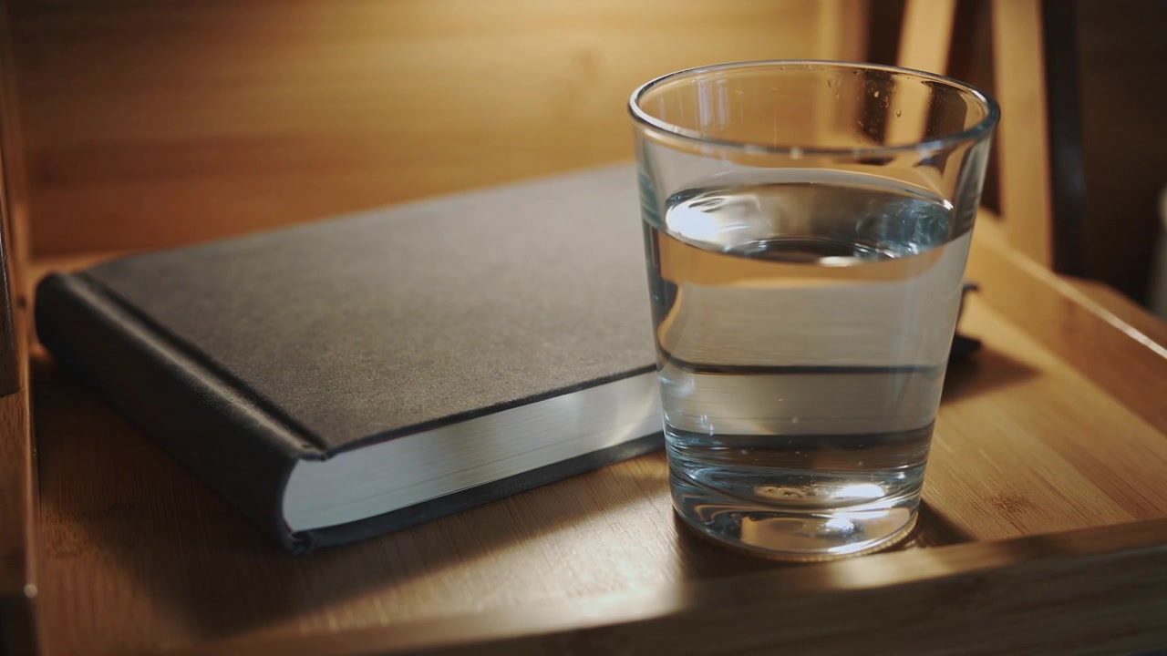 Bicchiere d'acqua su un vassoio di legno sul comodino, con un taccuino in evidenza e spazio per il testo.