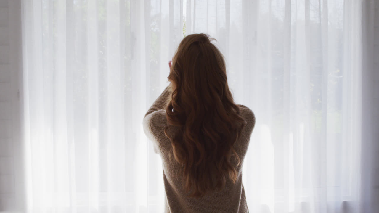 집 의 창문 의 커튼 을 그리는 여자 의 뒷면