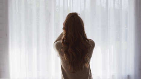 Rear-view-of-woman-drawing-curtains-of-the-window-at-home