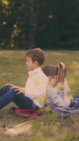 boys schoolmates tired of preparing for important tests sit leaning back to back on fresh lawn grass with books