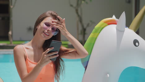 mujer usando el teléfono junto a la piscina con flotador unicornio