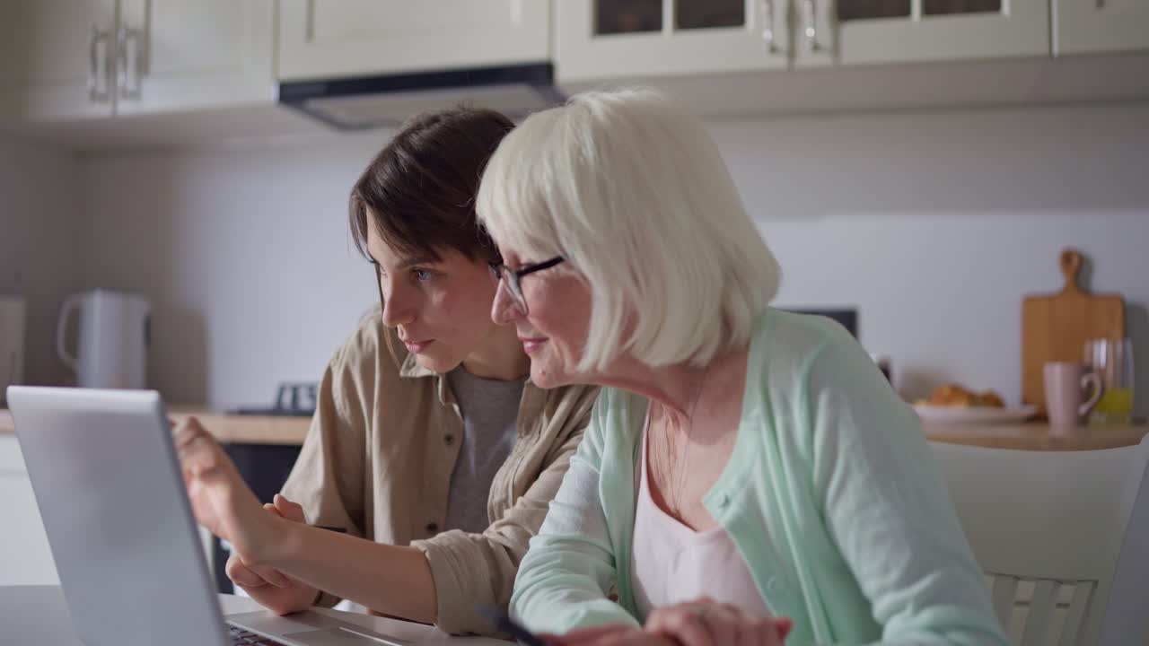 Grandmother and granddaughter using laptop together in kitchen
