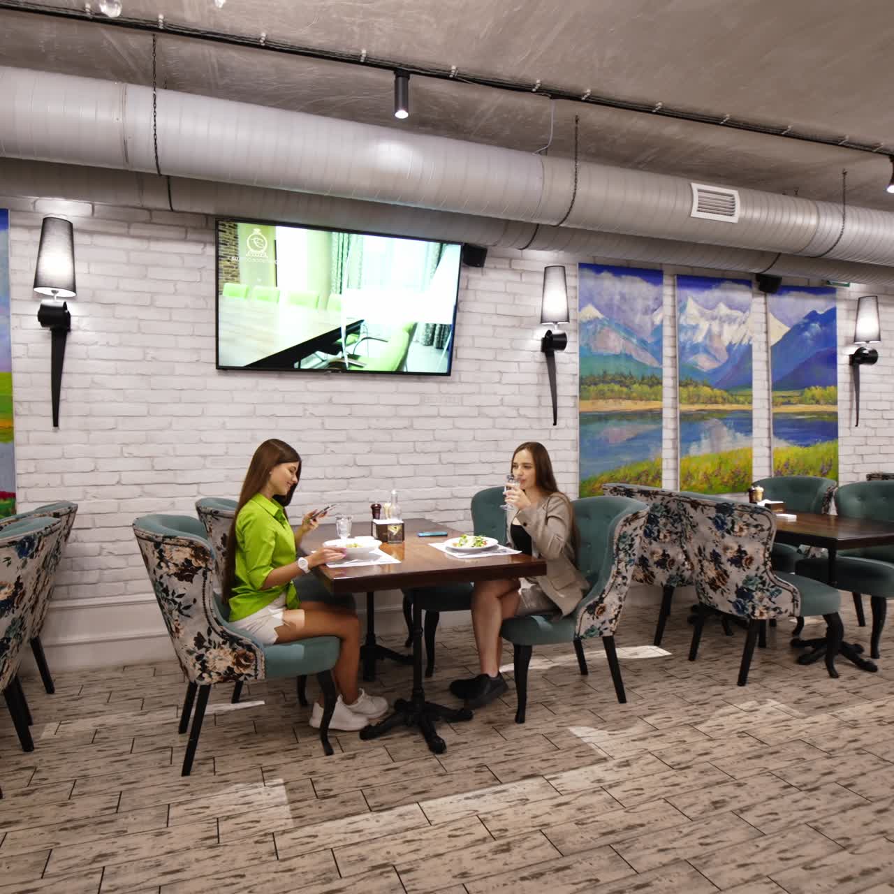 Young long-haired brunette girls came for dinner to a restaurant. Lady in green shirt takes a picture of her food on telephone. Slow movement to the couple dining at the next table