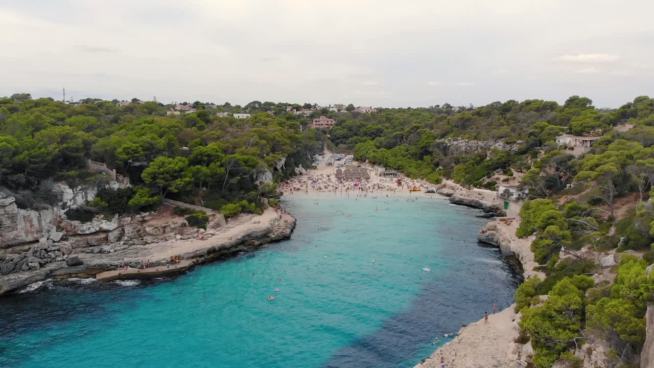 Dronebillede over turkisblåt vand med udsigt til travle Cala d'Or Strand