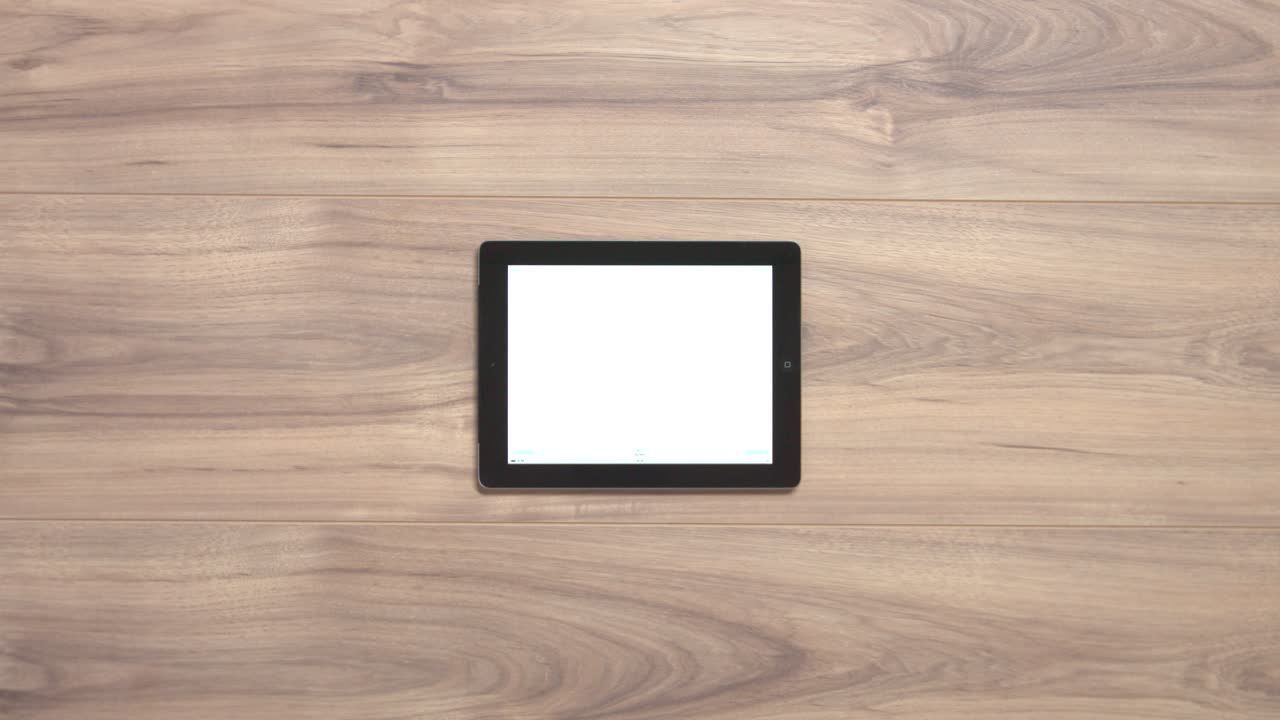 Two hands klicking a button on a white screen tablet and pulling it away from the wooden table