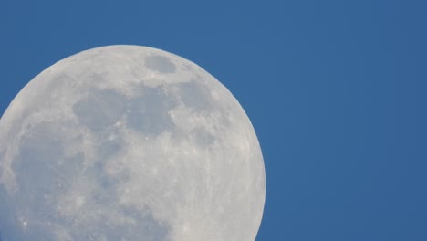 detailed footage of a full moon moving slowly against a clear blue sky showing the craters on the lunar surface