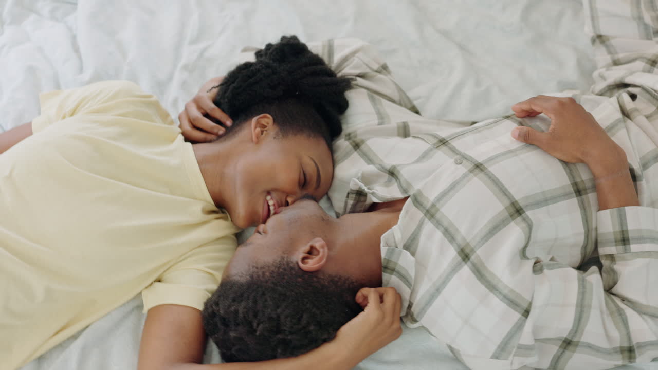 Couple, black woman and kiss on bed together