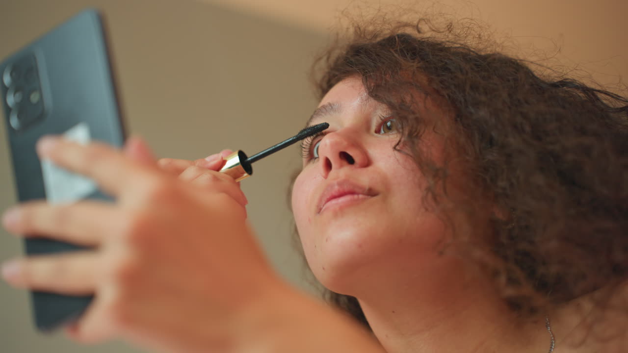 Donna che si trucca. Appassionata di bellezza che si prepara per la sera. Donna che applica con sicurezza il mascara nella camera d'hotel. Routine di cura personale femminile ripresa durante una sessione di tutorial di bellezza.