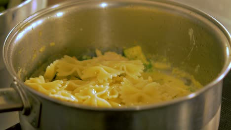 The-cook-tops-boiled-pasta-in-to-the-steel-pot-with-chicken-and-green-peas,-making-pasta-salad,-handheld-close-up-shot