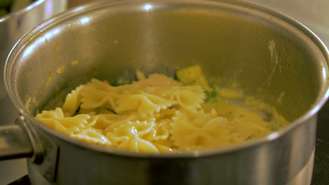 los cocineros cocinan pasta hervida en la olla de acero con pollo y guisantes verdes, haciendo ensalada de pasta, primer plano de mano