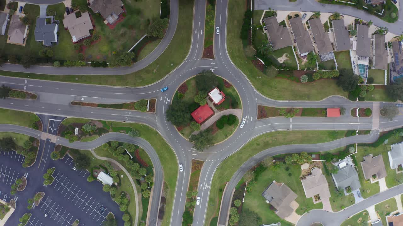 Aerial drone shot slowly rotating and rising above a roundabout in The Villages, Florida while cars drive along the road and clouds start to cover the view on a dreary day