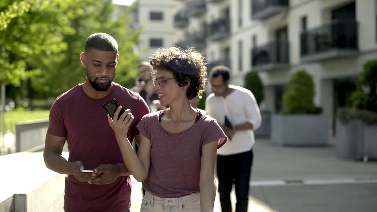 una joven pareja feliz caminando por la calle y mirando su teléfono inteligente.
