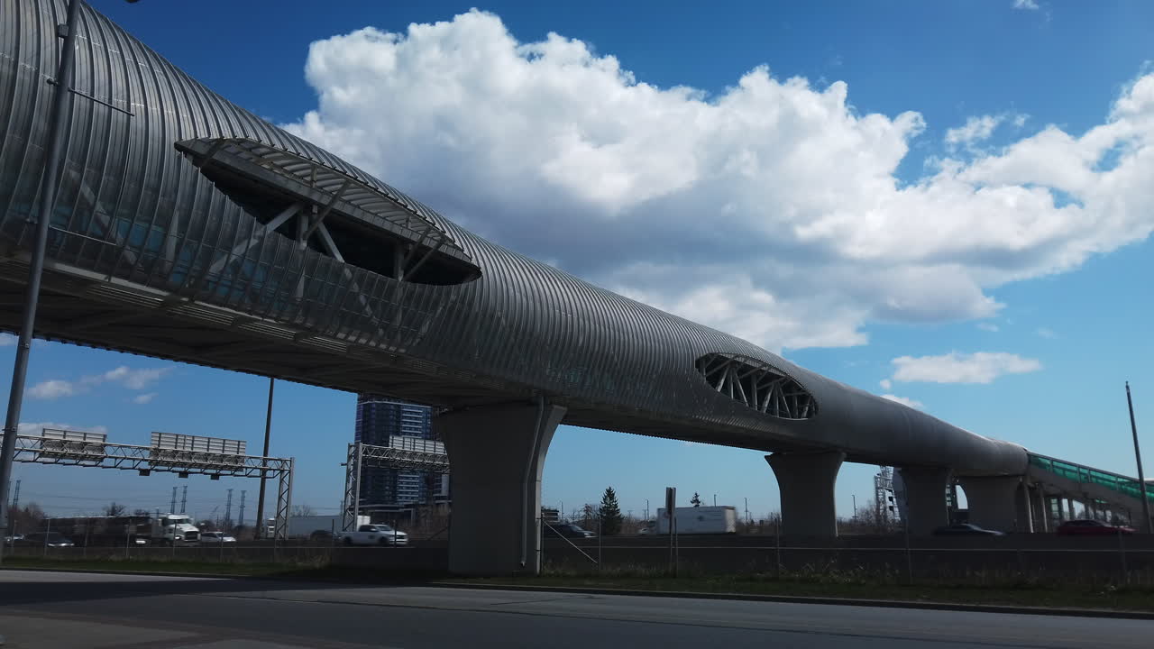 Fast highway traffic passing under a unique enclosed pedestrian bridge, wide shot