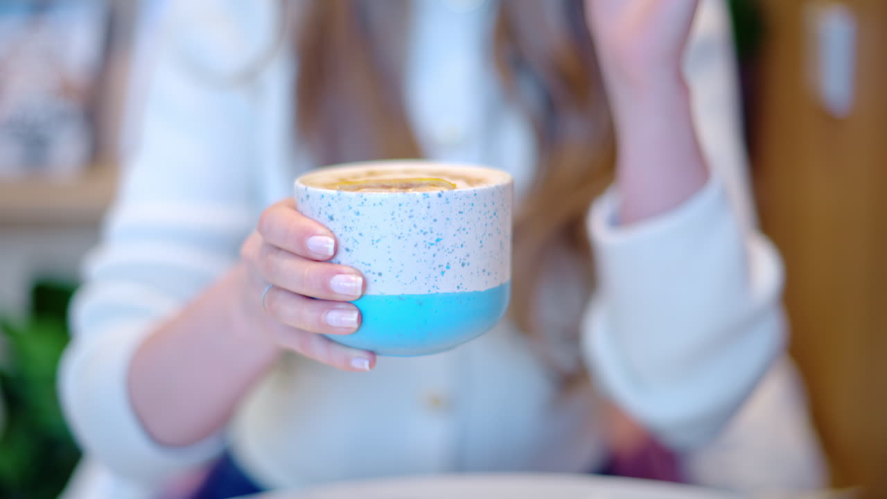 Woman drinking latte art coffee from ceramic cup in a cafe