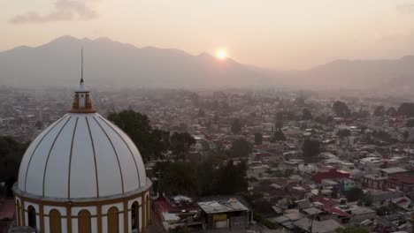 Drone-Pasando-Por-La-Iglesia-De-Guadalupe-Durante-La-Puesta-De-Sol-Inclinándose-Hacia-Arriba-Y-Mostrando-La-Ciudad-De-San-Cristobal-De-Las-Casas,-Chiapas,-México