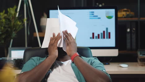 Closeup-disappointed-afro-businessman-getting-upset-with-papers-in-dark-office