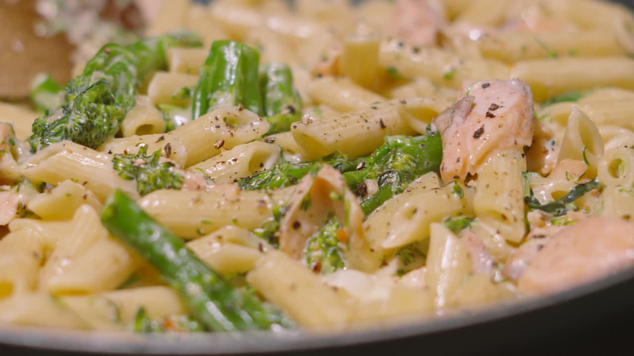 Close Up of Creamy Delicious Salmon and Broccoli Penne Italian Pasta with Cracked Black Pepper and Bubbling Creamy Sauce. Cooking Kitchen Seafood Healthy Eating Footage 4K.