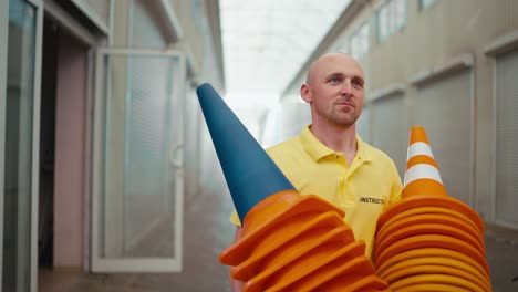 A-bald-man-with-blue-eyes-in-a-yellow-T-shirt-takes-orange-cones-out-of-his-garage-for-a-training-ground-in-a-motorcycle-school