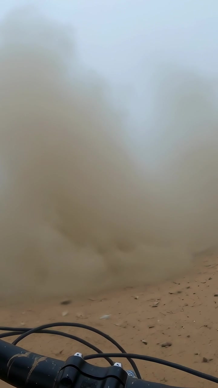 Video verticale: Nuvola di polvere che si solleva su un sentiero di sabbia vicino al manubrio o ai cavi di una bici, con il vento che soffia orizzontalmente.