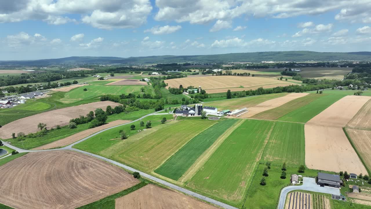 American farmers countryside with farmstead and cropland at cloudy day. Aerial backwards wide shot. Sunny day In spring season. Rural road in quiet rural area.